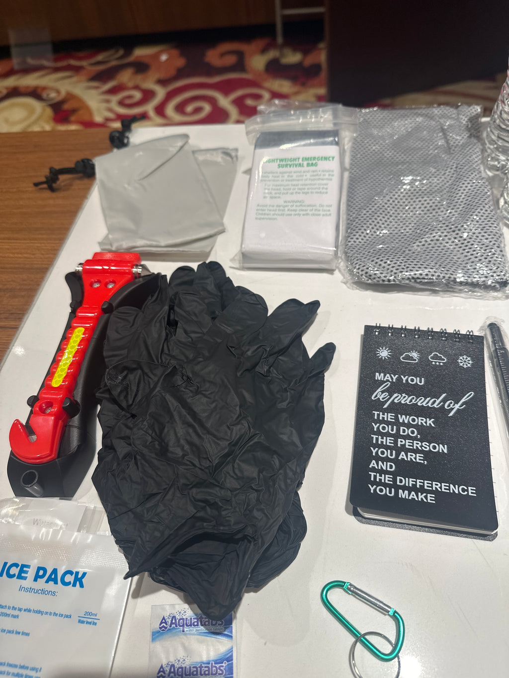Black gloves on a white surface with various items including a notebook and a tool.