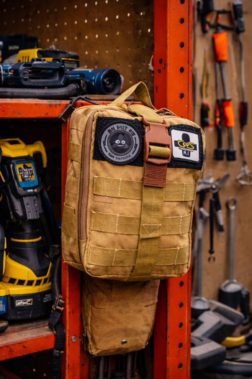 Tan backpack with tactical pouches hanging on a pegboard with tools in the background