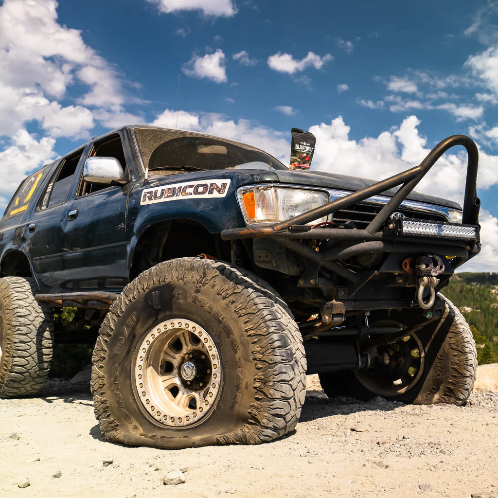Off-road vehicle with large tires on a dirt road under a blue sky with clouds.