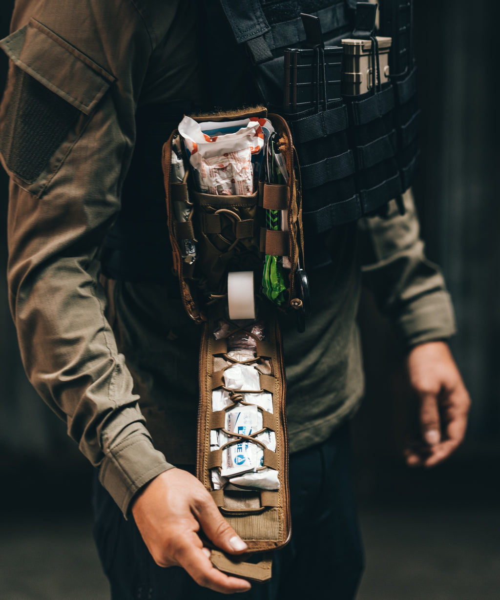 Person holding a tactical belt with supplies against a dark background