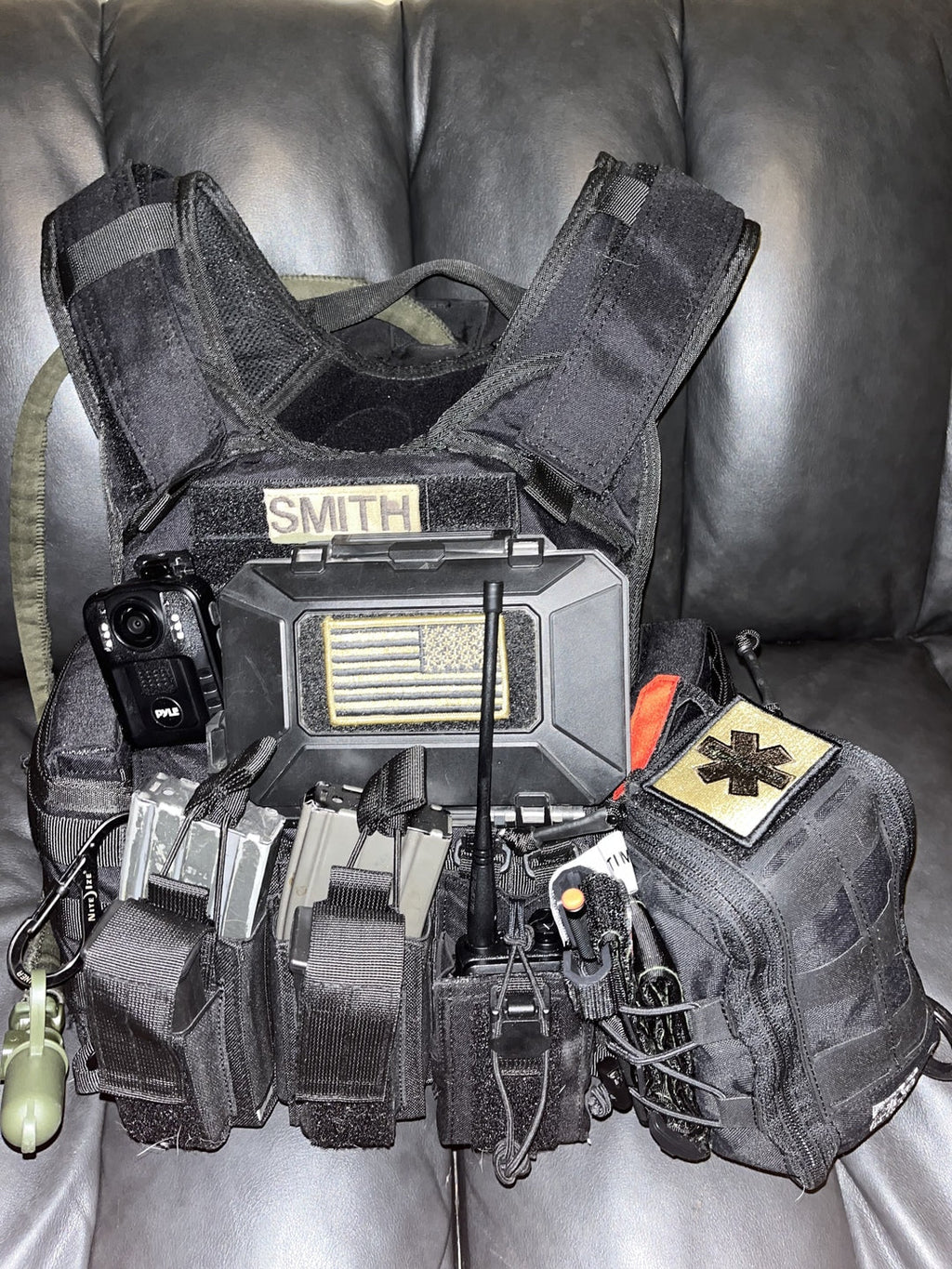 Black tactical vest with various equipment on a gray couch